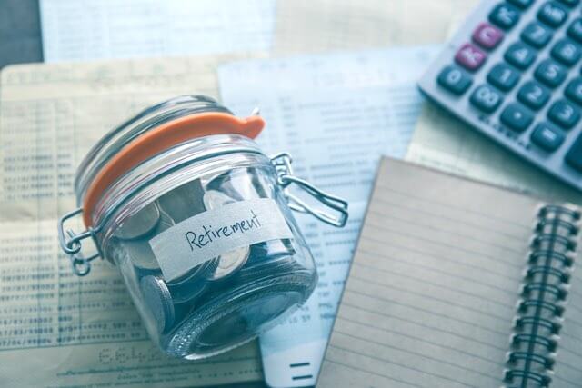 Glass jar lying on its side labeled 'retirement' next to a notebook and calculator on a desk depicting annuity/retirement savings