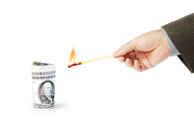 Close up of a businessman's hand holding a match as he moves to set fire to a roll of cash