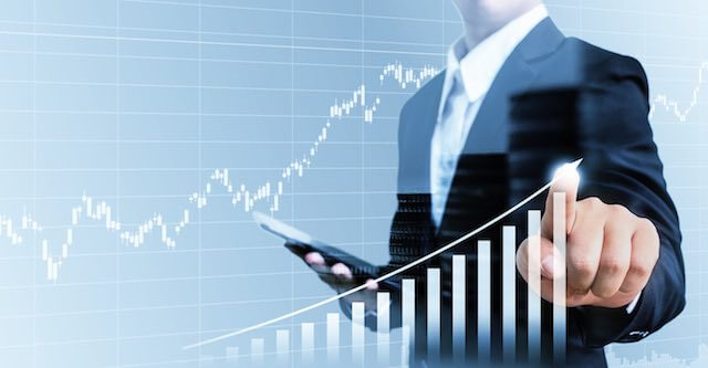 Businessman holding an iPad and touching the top of a rising bar graph on a touchscreen indicating a bull stock market/financial gains