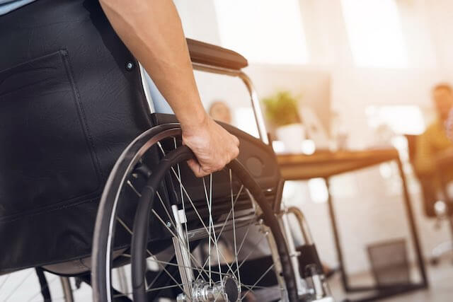 Close up of a man's hand pushing the wheel of a wheelchair in an office depicting disability, workplace benefits, disability retirement