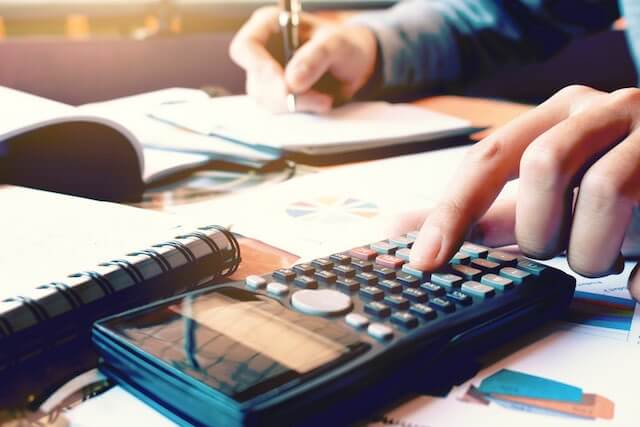 Close up of a woman's hands working on a calculator and writing notes as she performs financial calculations sitting at a desk