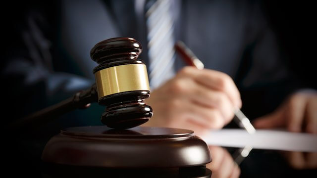 Close up of a wooden judge's gavel with a lawyer sitting at a desk in the background writing