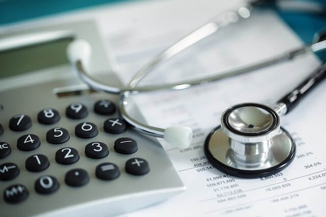 Calculator and stethoscope on top of a spreadsheet depicting health insurance premiums/costs