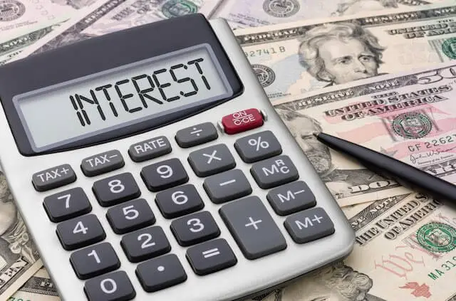 Calculator displaying the word 'interest' on its screen sitting on a spread of cash