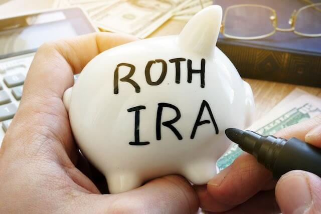 Close up of man's hands holding a piggy bank and writing 'roth IRA' on the side of it