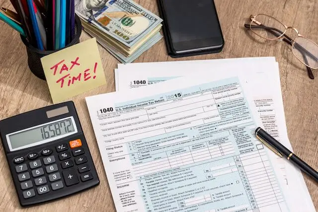 IRS income form 1040 sitting on a desk wit a pencil and a calculator along with a post it note that reads 'tax time'