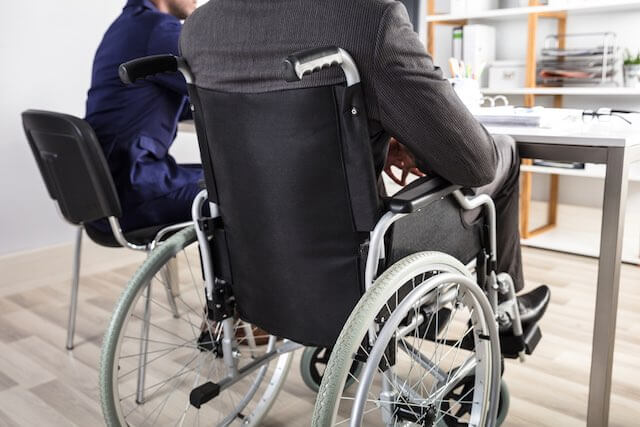 Businessman in a wheelchair viewed from behind as he sits at a conference room table in an office building - disability retirement, OWCP, workplace injury