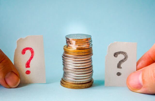 Stack of coins with two peoples' thumbs holding index cards with question marks on them on both sides of the coins depicting questions about money/salary