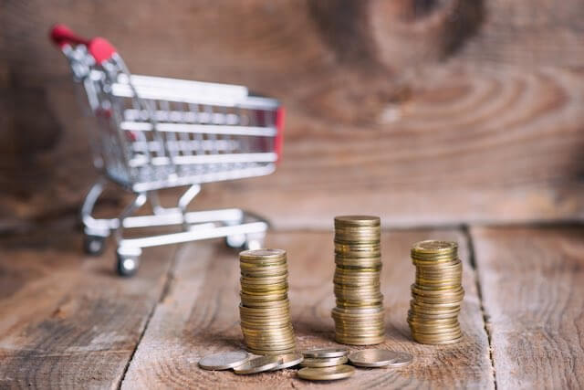 Shopping cart pictured in the background behind three vertical stacks of coins depicting the annual COLA/cost of living for federal retirees and Social Security recipients