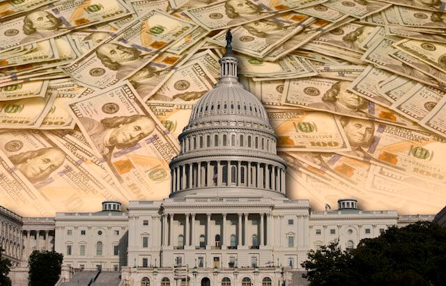 Congressional Capitol building in Washington, DC with a spread of cash pictured over and behind it depicting government spending