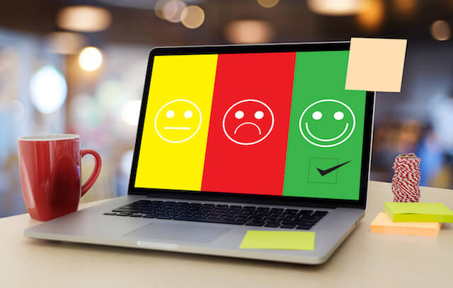Laptop computer with an indifferent, sad, and happy smiley emojis in the screen depicting employee job satisfaction ratings