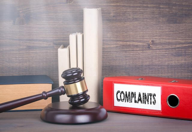 Judge's gavel on a desk next to a red binder labeled 'complaints'