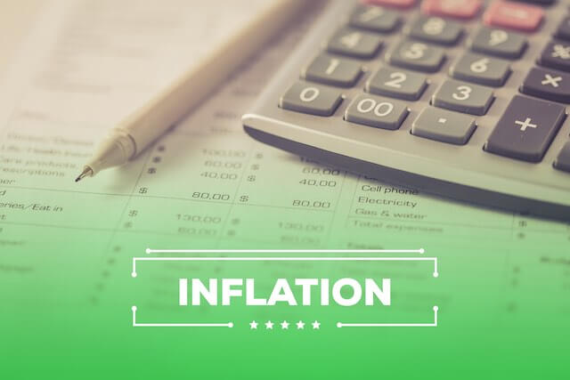 Word 'inflation' imposed over a picture of a spreadsheet on a desk with a pencil and calculator sitting on top of it