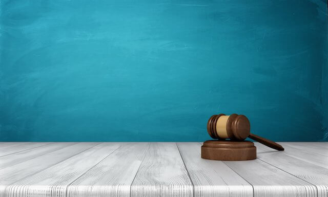 wooden judge's gavel sitting on grey floor against a turquoise blue background