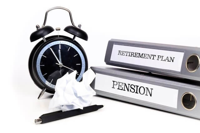 Old style alarm clock pictured next to two binders, one labeled 'retirement plan', the other labeled 'pension' against a solid white background depicting retirement planning