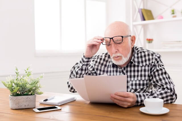 Senior citizen man sitting at a desk looking at bills with a puzzled look on his face