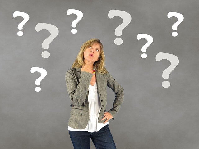 Woman looking perplexed standing in front of a group of white question marks on a gray background