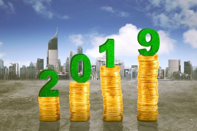 Stacks of gold coins increasing in size from left to right with the numbers 2019 over them pictured in front of a city skyline depicting 2019 locality pay raise/locality pay areas
