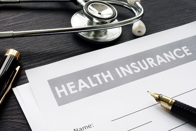 Documents on a desk labeled 'health insurance' sitting next to a pen and stethoscope, FEHB open season