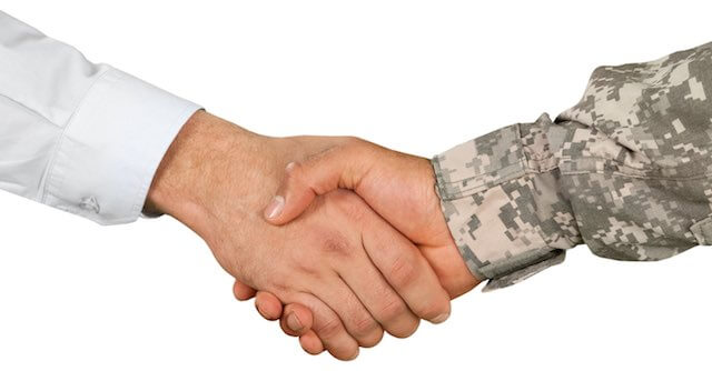 Close up of a handshake between a businessman and a military veteran in camouflage depicting veterans preference hiring in federal government