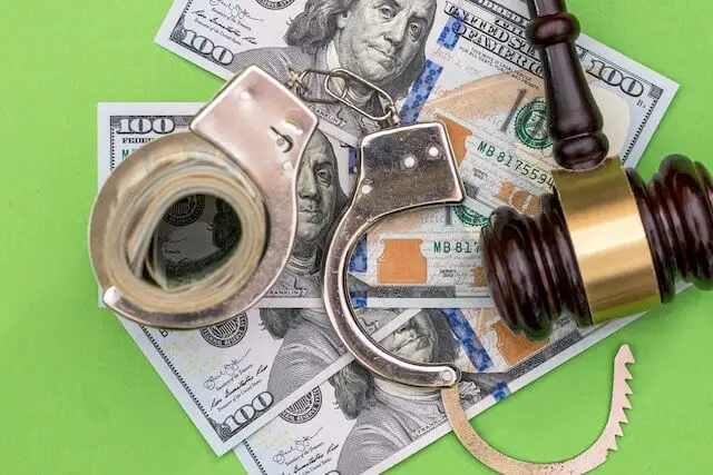 $100 bills, handcuffs and a judge's gavel sitting on a green background depicting a conviction of a money related crime