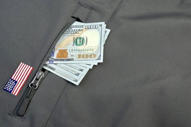 Several $100 bills sticking out of a military uniform coat pocket depicting military retirement, benefits, veteran