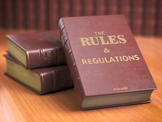 Stack of three law books on a desk with one facing the front that reads 'rules and regulations'