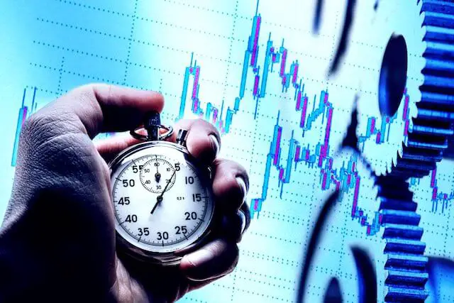 Close up of a man's hand holding a stopwatch against a background of financial charts depicting trying to time the stock market