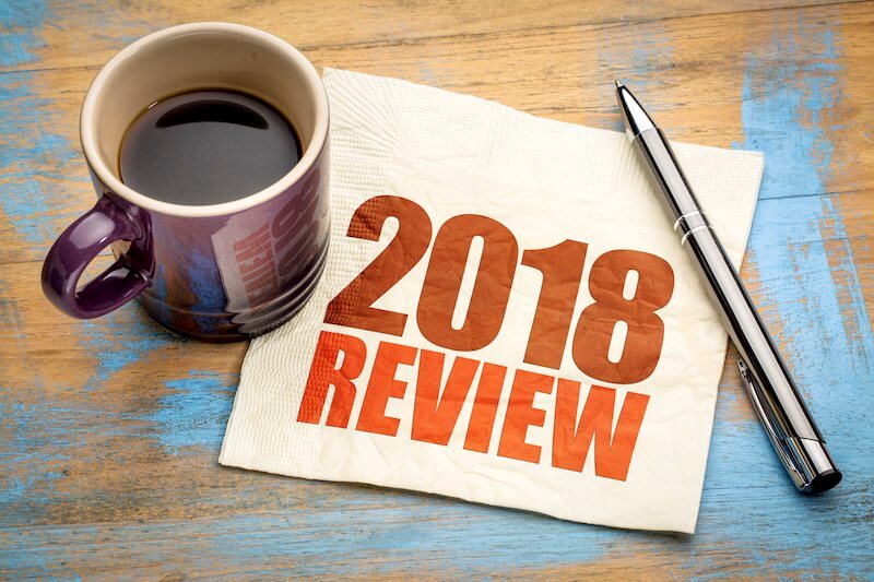 Coffee cup and a pen on a desk next to a paper napkin with the words '2018 review' written on it - year end, year in review for 2018