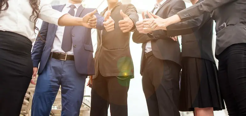 Close up of a group of business people in a huddle giving the thumbs up sign indicating happiness, collaboration and teamwork