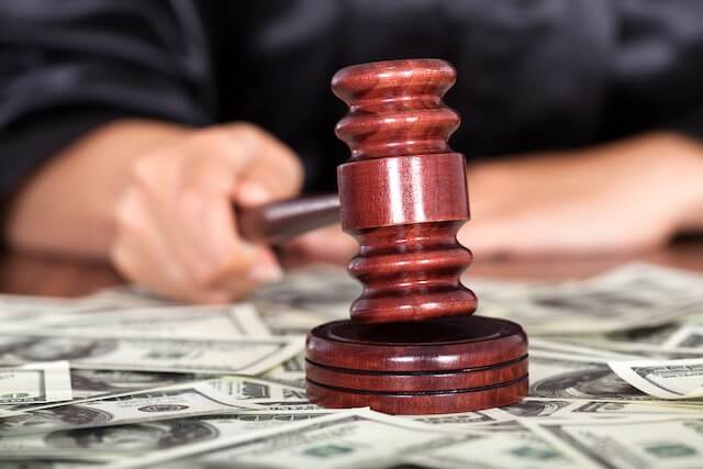Judge tapping his wooden gavel on its wooden base over a scattering of cash depicting a lawsuit for damages/compensation