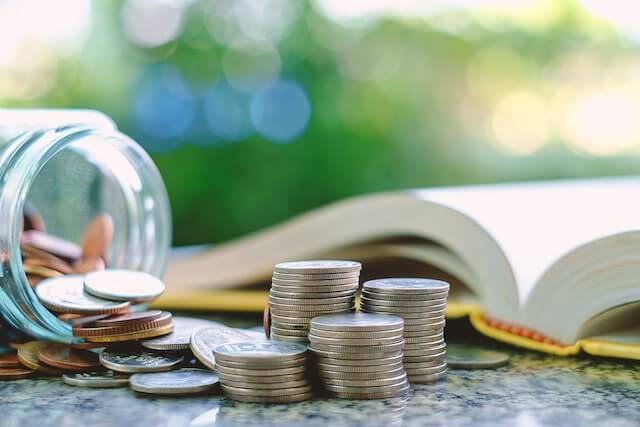 Jar of coins and stack of coins next to a book on a table depicting budgeting/financial planning