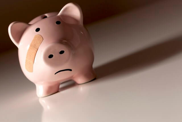 Pink piggy bank with a sad face and a bandage on its face depicting loss of money or wages