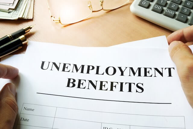 Sheet of paper on a desk labeled 'unemployment benefits' nexts to a calculator and glasses