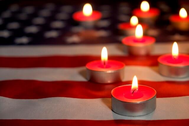 Several small red candles lit pictured over the display of a USA flag depicting mourning or a memorial service