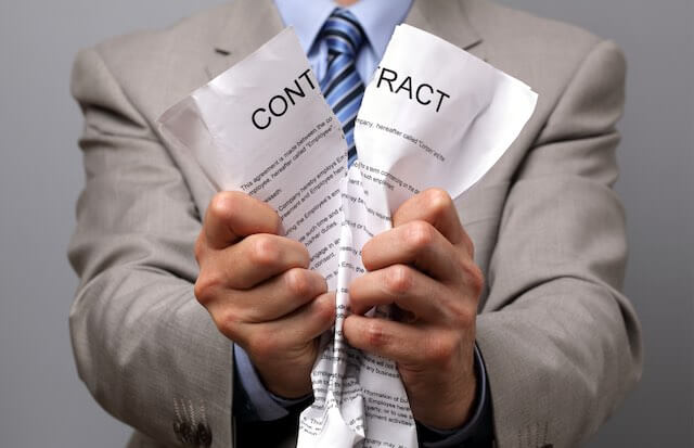 Businessman tearing a document between his hands that says 'contract' at the top