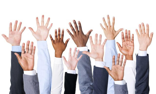 Close up of the arms of a group of businesspeople raised in the air in a show of unity