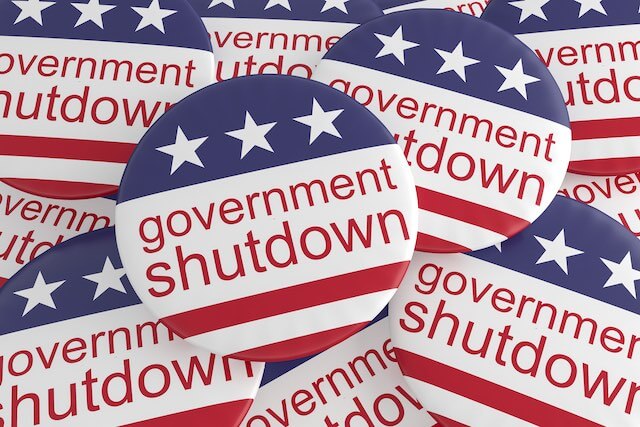Scattering of metal pin buttons that read 'government shutdown' with American flag design style/colors