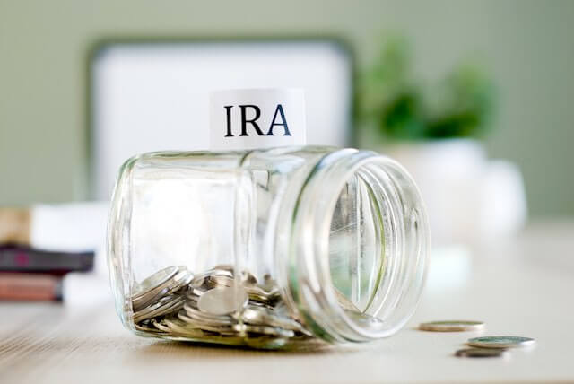 Glass jar labeled 'IRA' lying on its side filled with coins depicting retirement savings