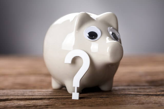Piggy bank on a wooden surface with a white question mark leaning up against it depicting money questions, possibility of a pay raise
