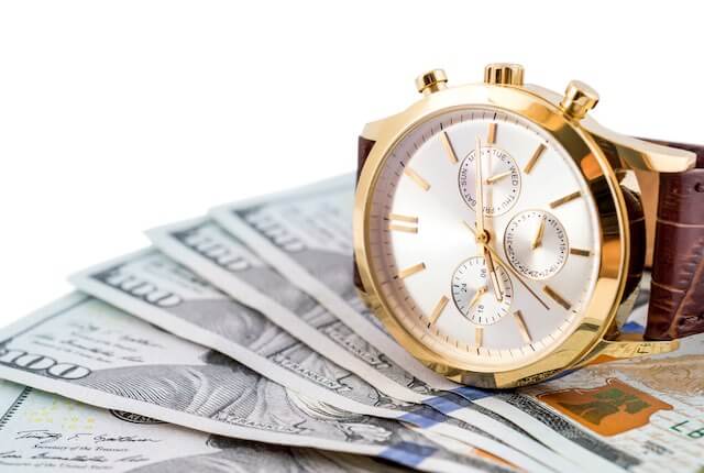 Wrist watch sitting on a spread of $100 bills - time is money, back pay