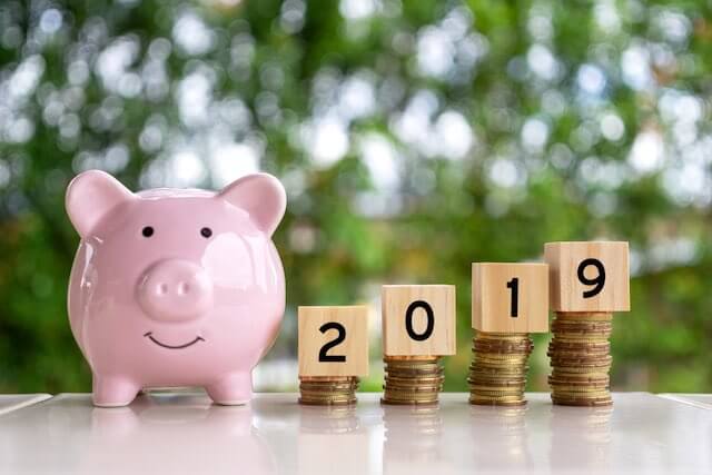 Pink piggy bank next to four stacks of coins that are progressively taller from left to right that have wooden numbers on top of them writing out 2019 depicting a 2019 pay raise or salary increase