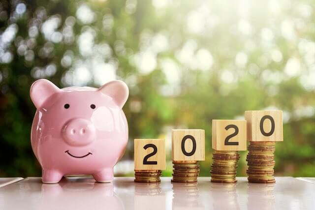 Pink piggy bank next to four stacks of coins that get progressively taller going from left to right topped with wooden blocks that spell out '2020' depicting a 2020 pay raise, salary increase