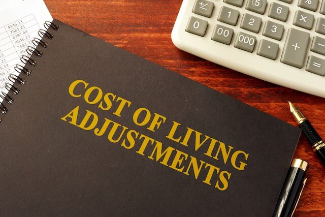 Notebook on a desk labeled 'cost of living adjustments' next to a calculator - COLA, FERS, CSRS retirement