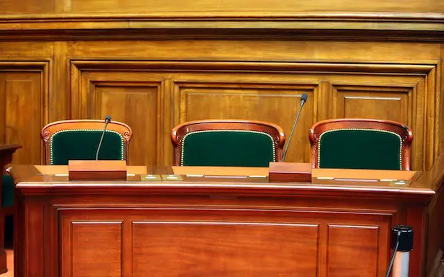 Three empty chairs behind a desk in a courtroom depicting judicial vacancies