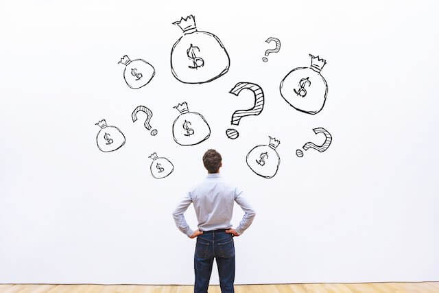 Man staring at a wall with illustrations of money bags and question marks depicting confusion and questions about pay/money/salaries/investing