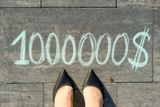 View of the tips of a businesswoman's feet standing on a sidewalk in front of the number '1,000,000$' written in chalk depicting a journey to becoming a TSP millionaire