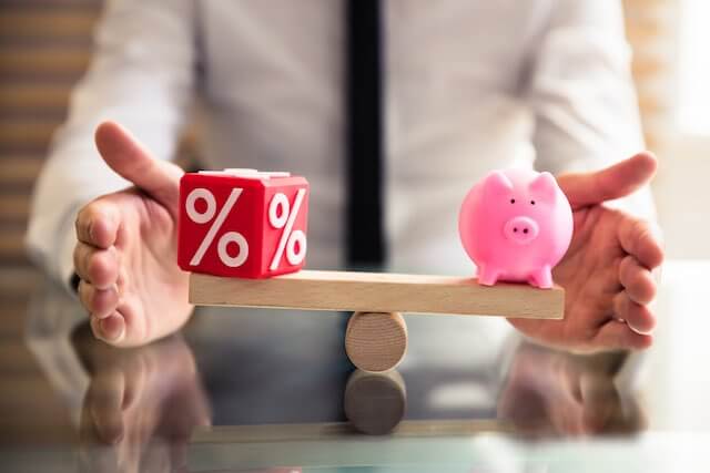 Man's hands helping balance a scale with a percentage on one side and a piggy bank on the other depicting a balance between locality pay percentages and pay raises