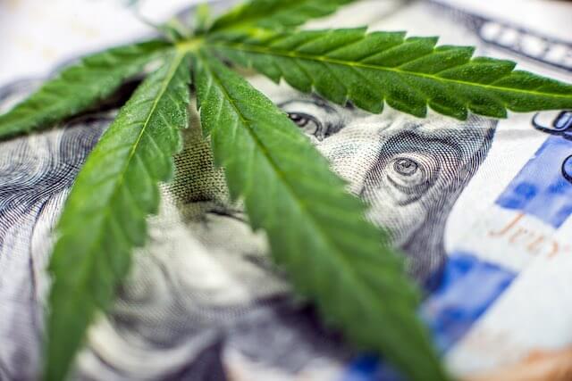 Marijuana leaf draped over the face of a $100 bill depicting cash money for drug trafficking