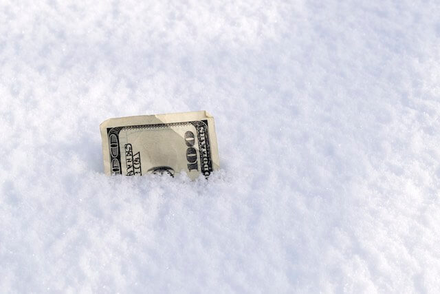 Tip of a $100 bill sticking up out of a snowbank depicting a pay freeze